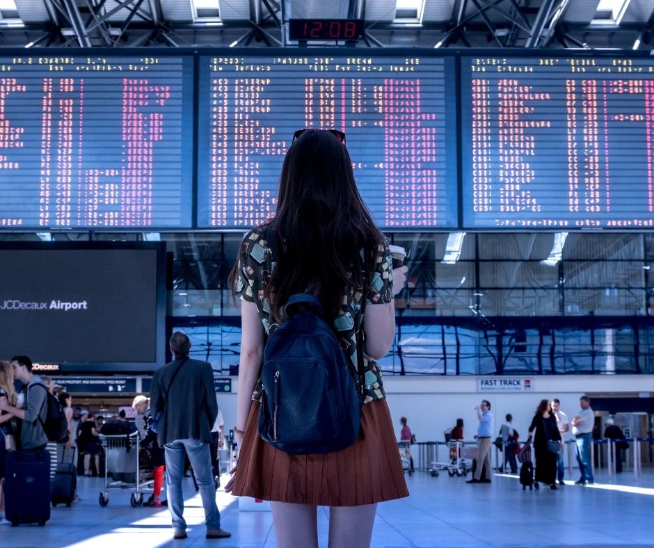 A young woman looks for her flight on the busy arrivals and departures boards at the airport.