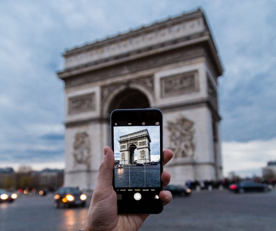 A personal taking a photograph on their smart phone of the Arc de Triomphe in Paris