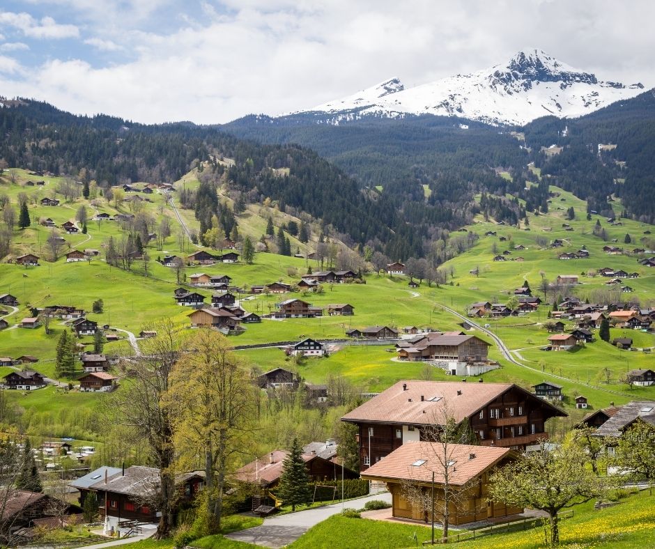 Beautiful Swiss valley with wooden chalets, and flanked by snowy mountains.